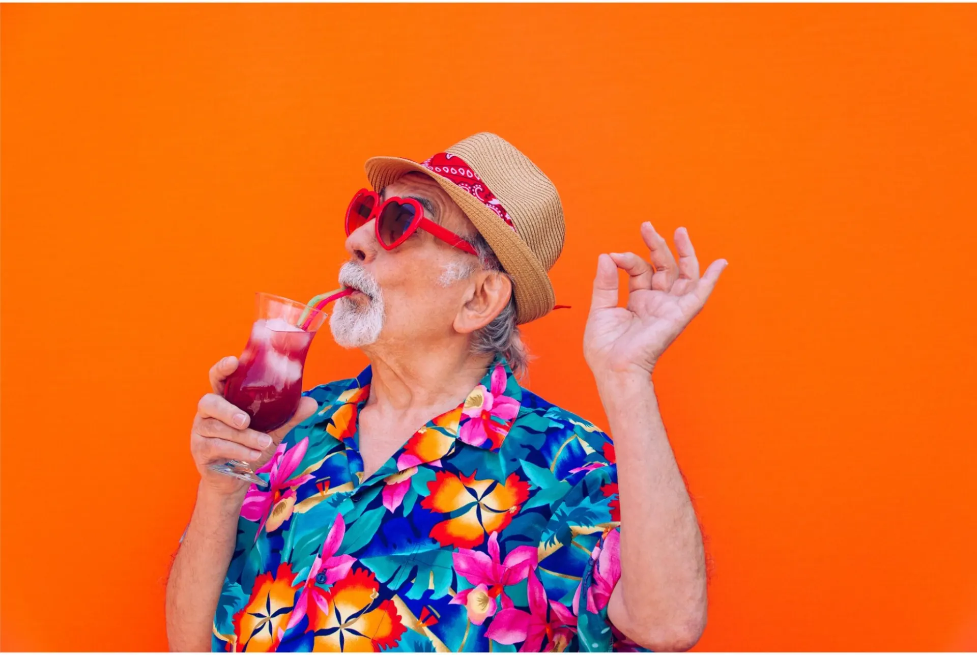 Man met hoed en zonnebril drinkt een cocktail voor een oranje muur
