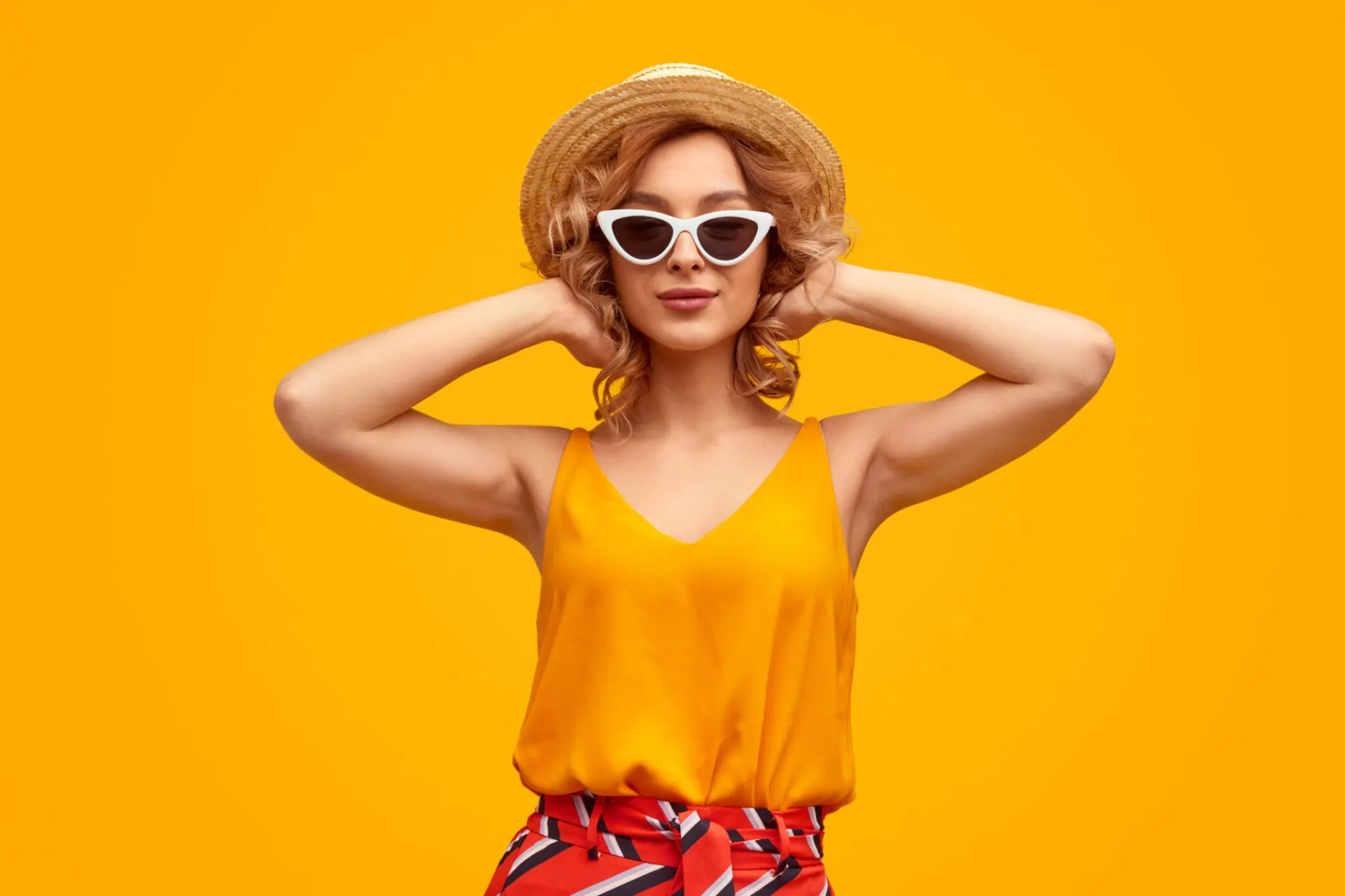 Vrouw met strohoed en zonnebril voor een gele muur